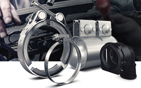 Metall-V-Bandschelle, Schlauchschelle und Kunststoff-Kabelhalterung vor unscharfem Montagehintergrund.