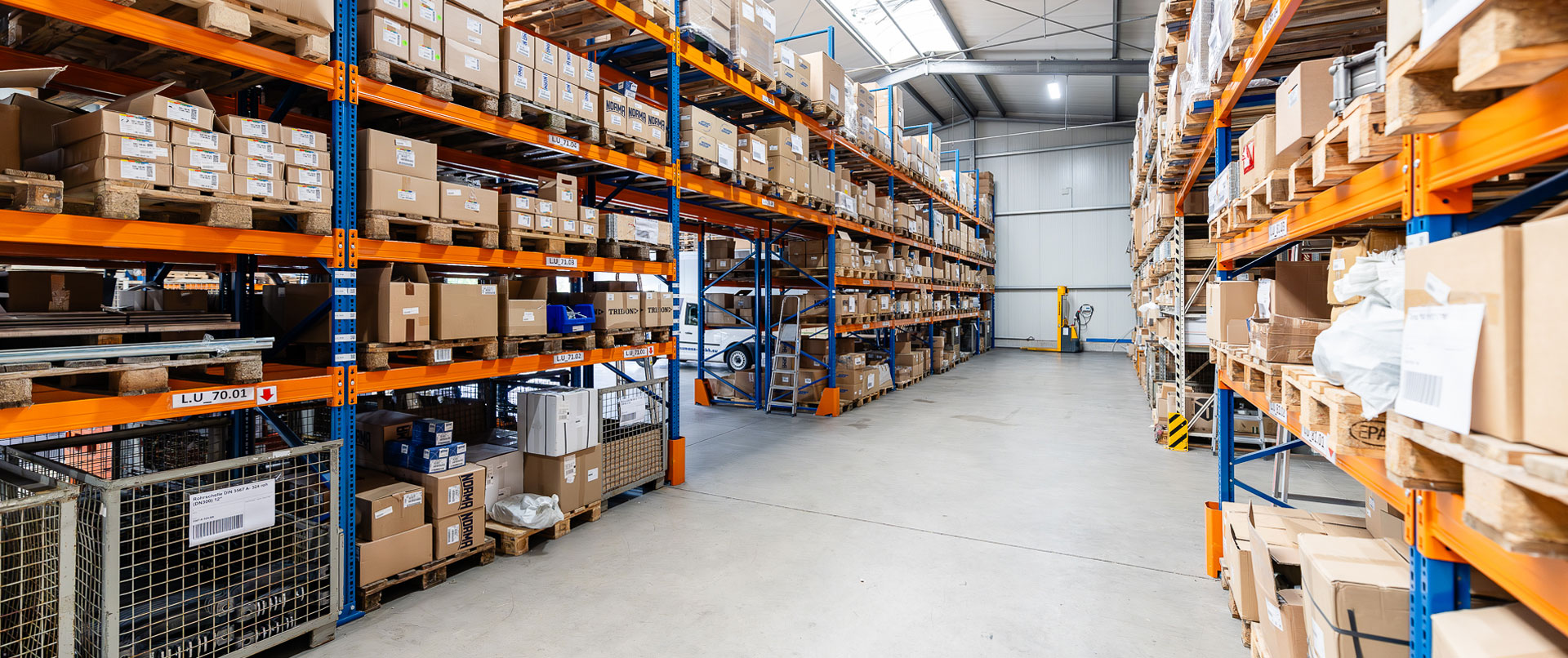 Gang zwischen Lagerregalen im Schellen-Shop, die mit diversen Rohrschellen, Schlauchschellen und Rohrverbindern gefüllt sind